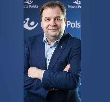 Sebastian Mikosz, menedżer, w garniturze z subtelnymi elementami lotniczymi i pocztowymi w tle, symbolizującymi jego karierę.