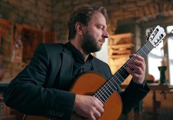 Marcin Dylla podczas dynamicznego występu na scenie w sali koncertowej, grający na gitarze klasycznej.