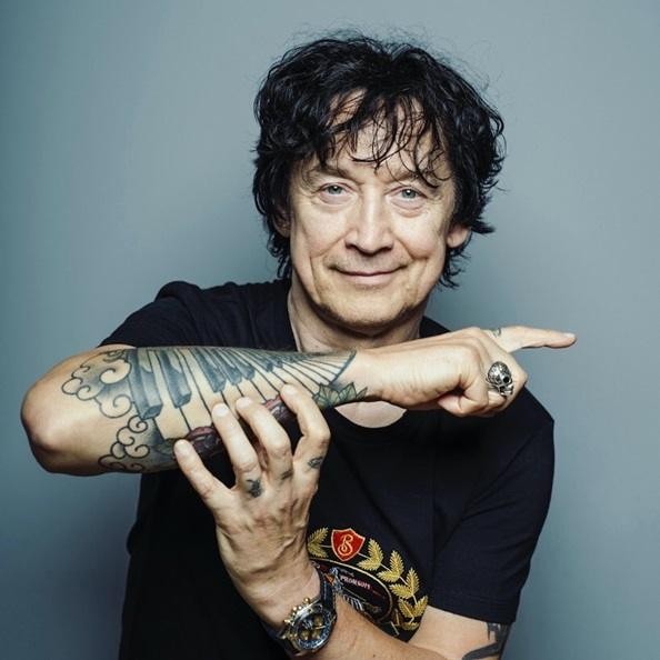 Jan Borysewicz strojący gitarę przed występem, w tle sprzęt muzyczny.