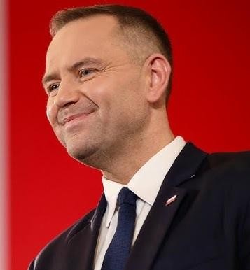 Karol Nawrocki w oficjalnym stroju, w tle instytucjonalne lub historyczne elementy, symbolizujące jego rolę prezesa IPN.