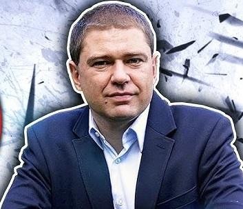Piotr Szumlewicz przemawiający na wiecu związkowym, z mikrofonem w dłoni i transparentami w tle, symbolizującymi walkę o prawa pracownicze.