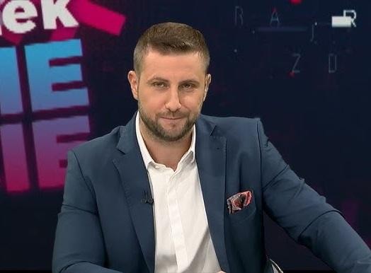Miłosz Kłeczek prowadzący program publicystyczny w studiu Telewizji Republika, dynamicznie gestykulujący.